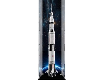 May include: A tall, vertical clear acrylic display case containing a model of the Saturn V rocket. The rocket is white with black sections, featuring the text USA and a small American flag. The background inside the case depicts outer space.