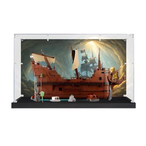 May include: A brown plastic model pirate ship displayed inside a clear rectangular acrylic case with a black base. The ship features tan sails, a skeleton figure at the stern, and small accessories on the base, set against a cave backdrop.