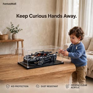 A young child is reaching for a model car displayed in a clear glass case on a wooden table.