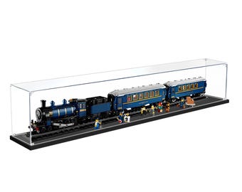 May include: A clear acrylic display case containing a blue and black toy steam locomotive with two matching passenger carriages on a black track base. Several small toy figures are positioned along the train, including passengers and staff.