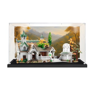 May include: A building block model of a house with green and white accents, featuring a tiled roof, a balcony, and a white domed gazebo structure. The model is enclosed in a clear rectangular display case with a black base against a mountain backdrop.