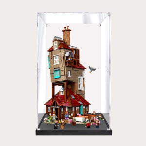 May include: A tall, multi-story building constructed from brown, tan, and red plastic bricks, enclosed in a clear acrylic display case. The structure features an asymmetrical, leaning design with multiple windows, a chimney, and several small minifigures.
