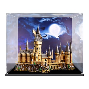May include: A detailed brick-built castle model featuring tan walls, grey conical roofs, and multiple towers, enclosed in a clear acrylic display case. The background depicts a dark blue night sky with a bright full moon and flying silhouettes.