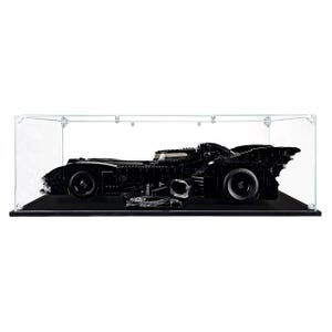May include: A black Batmobile model car constructed from building blocks, displayed inside a clear rectangular acrylic protective case. The vehicle features a low-profile design, large wheels, and a small black plaque with text positioned at the front.
