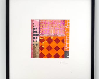 May include: Abstract art piece in a black frame. The artwork features a collage of colors and patterns, including pink, orange, red, and gold. The design incorporates geometric shapes and textures, with a signature in the bottom right corner.