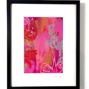 May include: Abstract art print in a black frame with a white mat. The artwork features a vibrant mix of pink, red, silver, and gold colors. The painting has a textured appearance with visible brushstrokes and scribbled lines. Signed in the bottom right corner.