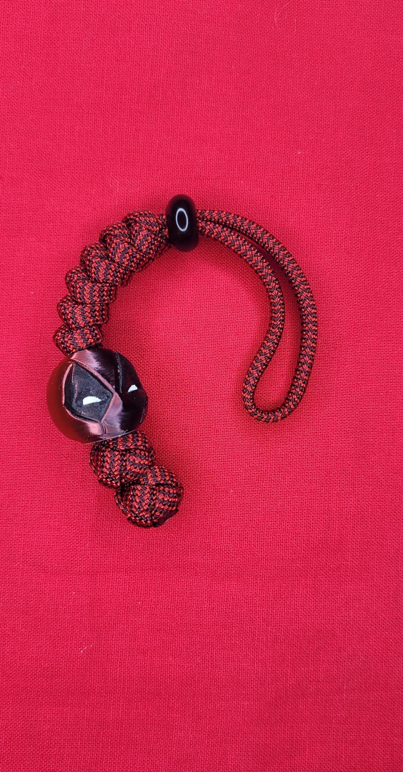 Puede incluir: Un cord&oacute;n rojo y negro con un dije de m&aacute;scara de Deadpool. El dije es negro con detalles de ojos blancos. El cord&oacute;n est&aacute; hecho de cord&oacute;n trenzado rojo y negro, con una cuenta y un lazo negros.