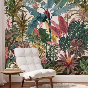 Peut inclure: Un fauteuil capitonné blanc avec une structure en bois repose sur un tapis rond à franges à côté d'une petite table d'appoint en bois. Le mur derrière présente une fresque murale de jungle tropicale dense avec des palmes vertes et des fleurs roses.