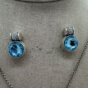 May include: A silver necklace with a pendant and matching earrings. Each piece features a large, round, light blue gemstone. The top of each earring and pendant is decorated with small, clear crystals.