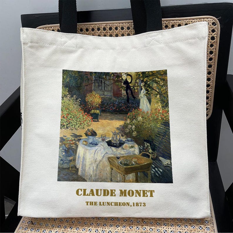 May include: A white canvas tote bag with a painting of a luncheon scene by Claude Monet. The painting depicts a group of people gathered around a table in a garden setting. The text "Claude Monet, The Luncheon, 1873" is printed below the painting.