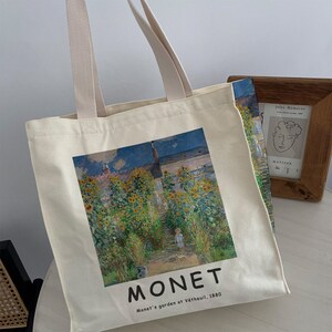 May include: A white canvas tote bag with a printed image of a painting by Claude Monet. The painting depicts a garden with sunflowers and a path leading up to a house. The text "MONET" and "Monet's garden at V&eacute;theuil, 1880" is printed below the image.