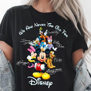 May include: Black t-shirt featuring a colorful graphic of Disney characters including Mickey Mouse, Minnie Mouse, Donald Duck, Daisy Duck, Goofy, and Pluto. The text "We Are Never Too Old For Disney" is printed above the characters, with the Disney logo below.