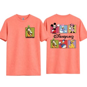 May include: Coral-colored t-shirt featuring Goofy in a green-bordered square on the front, with the name "CHRISTOPHER" below. The back displays Mickey Mouse, Daisy Duck, Minnie Mouse, Goofy, Donald Duck, and Pluto in squares, with "Disneyland" text.