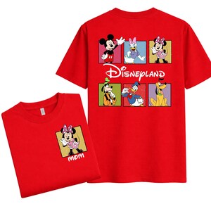 May include: Red t-shirts featuring Disney characters. One shirt has a Minnie Mouse graphic with the word "mom" on the front. The other shirt has a Disneyland logo and character graphics on the back, including Mickey Mouse, Daisy Duck, and Pluto.