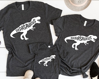 May include: A set of three gray t-shirts with a dinosaur silhouette and the words "Dadasaurus", "Mamasaurus", and "Babysaurus" printed in white.