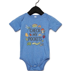 May include: Blue baby bodysuit with the text "CHECK MY POCKETS" and illustrations of a dragonfly, leaves, mushrooms, berries, and a caterpillar. The bodysuit is hanging on a black hanger.
