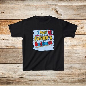 Op de afbeelding: Zwart T-shirt met een blauwe, gele, rode en witte afbeelding met de tekst "I must be about my Father's Business Luke 2:49".