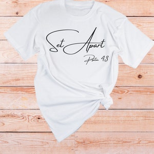 May include: White t-shirt with black text that reads "Set Apart Psalm 4:3".