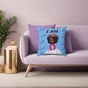 Puede incluir: Una almohada azul con una ilustración de dibujos animados de una niña con una corona de flores. El texto "I AM" está por encima de la niña y las palabras "Amazing, Excellent, Intelligent, Courageous, Gifted, Kind, Loving, Happy, Brilliant, Joyful, Fantastic, Deserving, Hopeful" están dispuestas alrededor de la niña en un círculo.