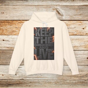 May include: A cream-coloured hoodie with a graphic print of the text "KEEP THE COMMANDMENTS AND LIVE" in a cracked, stone-like design with orange lightning bolts.