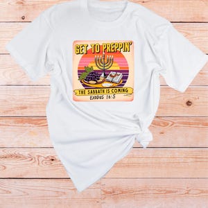 Könnte beinhalten: Weißes T-Shirt mit einem Grafikdesign, das einen Sonnenuntergang, eine Menora, Trauben, Brot und den Text "Get to Preppin' The Sabbath is Coming Exodus 16:5" zeigt