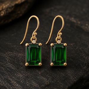 Peut inclure: Une paire de boucles d'oreilles pendantes en or avec des pierres vertes rectangulaires taille émeraude. Chaque boucle est suspendue à un crochet en or incurvé et ornée d'une petite pierre ronde transparente fixée au-dessus de la pierre verte.