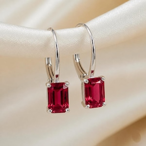 Peut inclure: Une paire de boucles d'oreilles créoles argentées ornées de pierres précieuses rectangulaires rouge foncé taille émeraude, fixées par quatre griffes. Les boucles présentent un fermoir à levier articulé et une finition métallique polie.