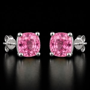 May include: A pair of stud earrings featuring cushion-cut pink gemstones set in silver-toned metal. Each earring has four prongs securing the stone and includes a matching silver-toned metal butterfly back closure for secure wear.