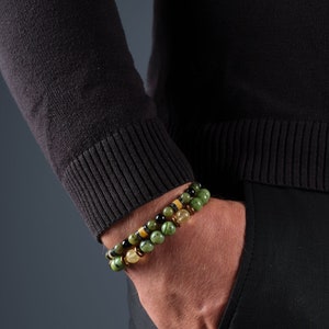 May include: Two beaded bracelets on a wrist. The bracelets are made of green, black, and gold beads.