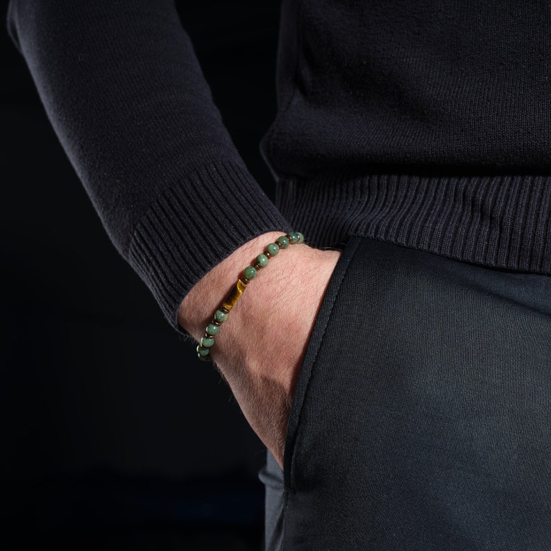 A green jade stone and a yellow hematite stone bracelet on the men's wrist, flat in the middle of the bracelet, adds elegance to the shiny tiger's eye stone