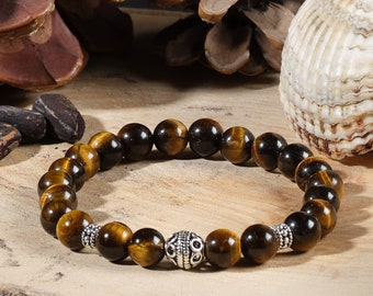 May include: A beaded bracelet featuring tiger's eye gemstones. The bracelet has a mix of dark brown and golden-brown beads, with a decorative silver bead in the center. The bracelet is strung on an elastic band.