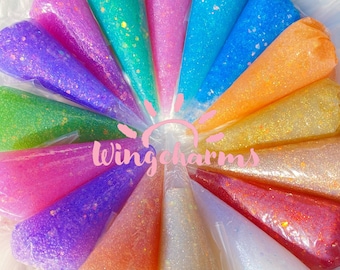 May include: Assortment of 15 colourful glitter glue tubes in cone-shaped packaging. Each tube features a different colour and glitter combination. The tubes are arranged in a circle with the brand name "Wingcharms" in the centre.