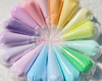 May include: A selection of colourful icing bags arranged in a circular pattern. The bags contain pastel-coloured frosting in shades of pink, purple, blue, green, yellow, and orange. The image includes the text "Wingcharms".