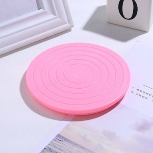 May include: Pink plastic turntable with concentric circles and numbers 2, 1, 0, 8, 6, 7, 4, 3, 2, 1, 0 printed on the surface. This turntable is used for rotating cakes or other baked goods.