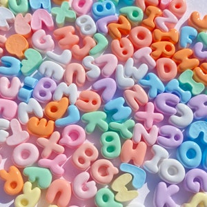 May include: A collection of colorful plastic letter beads in pastel shades of pink, blue, green, yellow, and white. The beads are shaped like letters of the alphabet and are perfect for crafting projects.