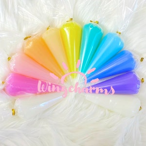 May include: A rainbow assortment of ten clear plastic cones filled with colorful slime. The cones are arranged in a semi-circle with the text "Wingcharms" in pink letters in the center.