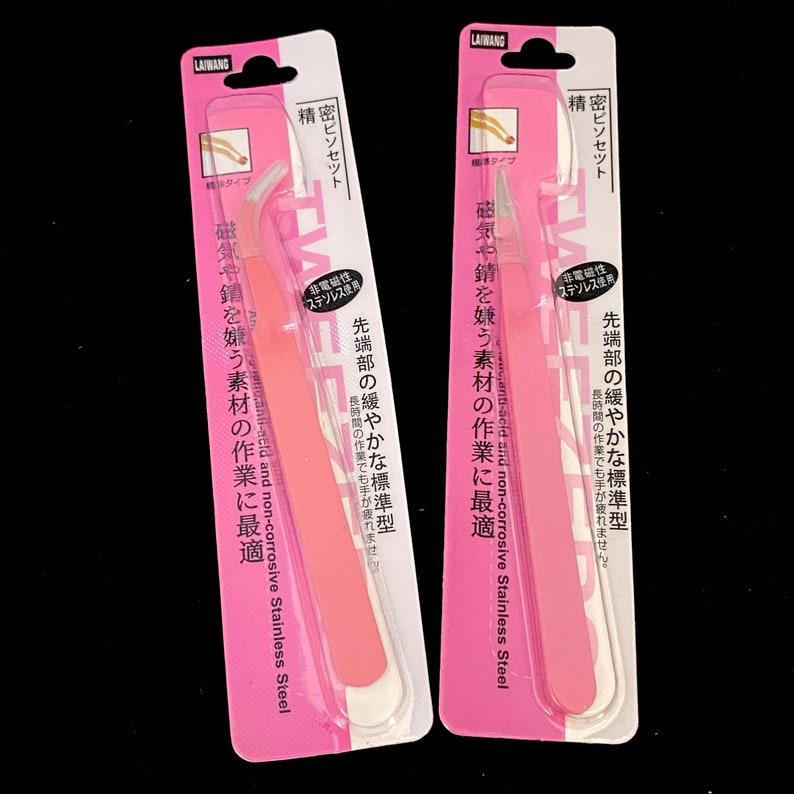 Puede incluir: Dos pinzas de depilar rosas empaquetadas en cart&oacute;n blanco y rosa. El empaque incluye texto japon&eacute;s que dice "anti&aacute;cido y no corrosivo Acero inoxidable" y "resistente al magnetismo y a la oxidaci&oacute;n".