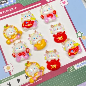 May include: Eight white resin charms with a cartoon deer design. Each charm features a different Chinese New Year symbol, including a gold ingot, a red envelope, and a fish. The charms are approximately 1 inch in size.