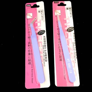 Puede incluir: Dos pares de pinzas con embalaje rosa. Las pinzas est&aacute;n etiquetadas con "精密ピンセット", que se traduce como "pinzas de precisi&oacute;n" en ingl&eacute;s. El embalaje tambi&eacute;n incluye el texto "非電磁性", que se traduce como "no magn&eacute;tico" en ingl&eacute;s. Las pinzas est&aacute;n hechas de acero inoxidable y est&aacute;n dise&ntilde;adas para trabajos de precisi&oacute;n.