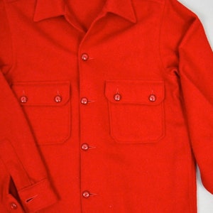 May include: A red wool shirt with a button-up front and two large pockets. The shirt has a classic, workwear style.