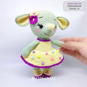 May include: A crocheted green and yellow doll with a purple flower on its head. The doll is wearing a yellow dress with a purple trim and colorful beads. The doll is standing on a white surface.  YOUR PHOTOS INSTAGRAM @lenny_cu