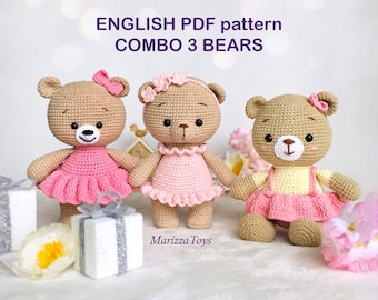 May include: Three crocheted teddy bears wearing pink and yellow dresses. The bears have brown fur, black eyes, and pink noses. The bears are sitting on a white surface with a white gift box and a pink flower.