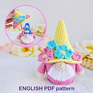 May include: A crocheted gnome figure with a yellow hat decorated with blue and pink flowers. The gnome has a pink body and a white beard. The image shows a small opening to hold treats. The image also includes a smaller inset showing the gnome holding a chocolate treat.
