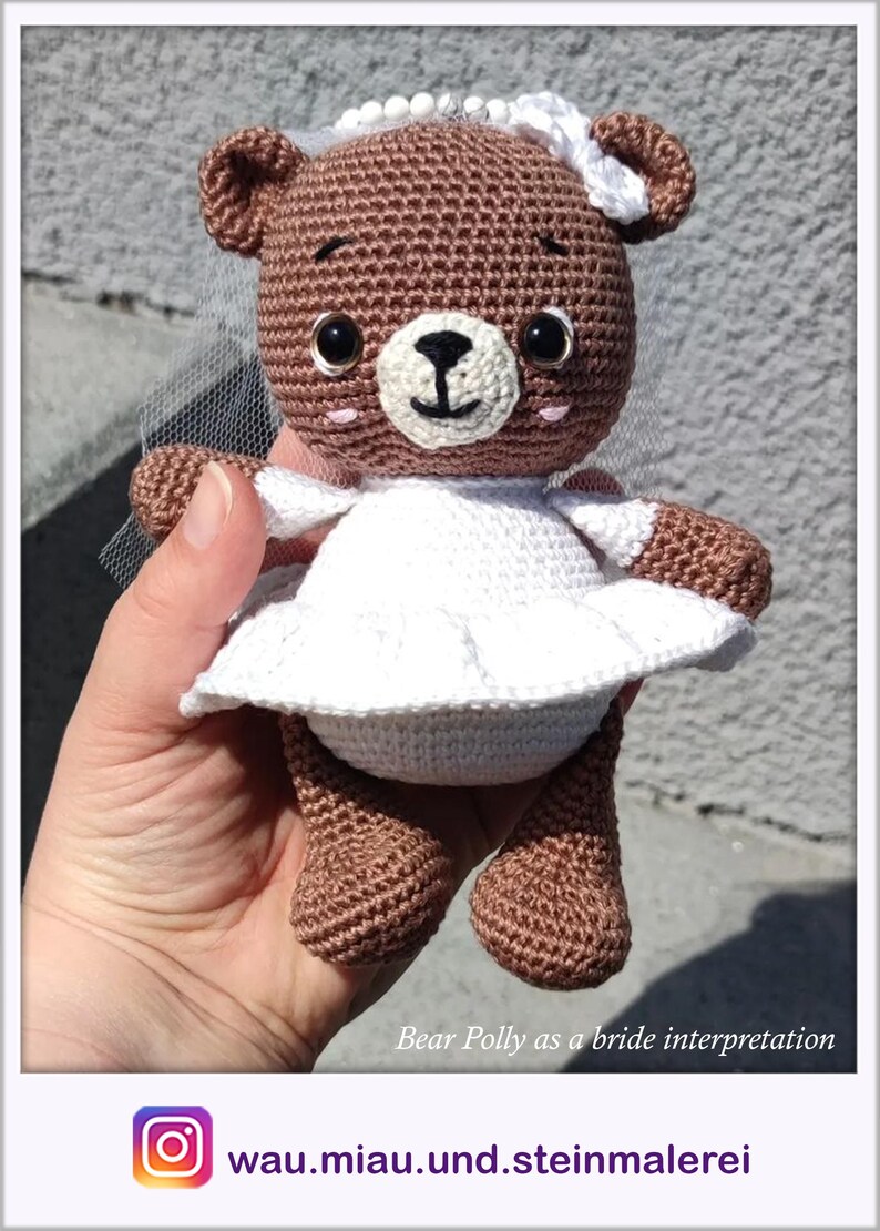 May include: A brown crocheted teddy bear wearing a white crocheted dress and veil. The bear has black eyes and a pink nose. The bear is being held by a hand.