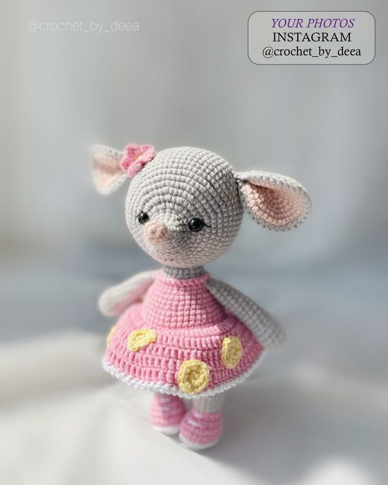 May include: A gray crocheted stuffed animal with pink ears and a pink dress with yellow polka dots. The animal has a pink flower on its head and black eyes.