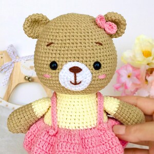 May include: A crocheted brown bear wearing a yellow and pink dress with a pink bow on its head.