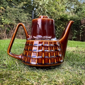 May include: A brown ceramic teapot with a square patterned design. The teapot has a spout and a handle.