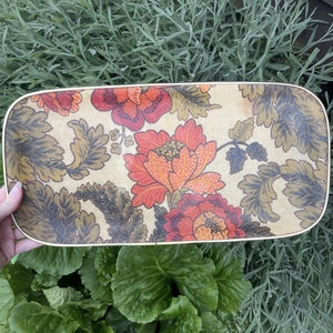 May include: A rectangular serving tray with a floral pattern in shades of red, orange, and green. The tray has a cream-coloured background and a gold-coloured rim.