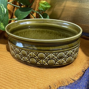 Puede incluir: Un tazón grande de cerámica verde con un patrón geométrico de círculos y triángulos. El tazón está sobre una superficie marrón.