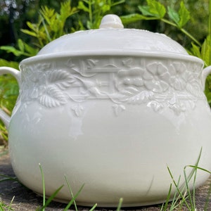 May include: White ceramic serving dish with a lid and two handles. The dish features an embossed floral design.